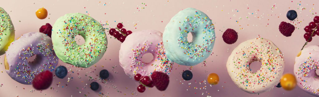 Sweet and colourful doughnuts with sprinkles and berries falling or flying in motion against pink pastel background